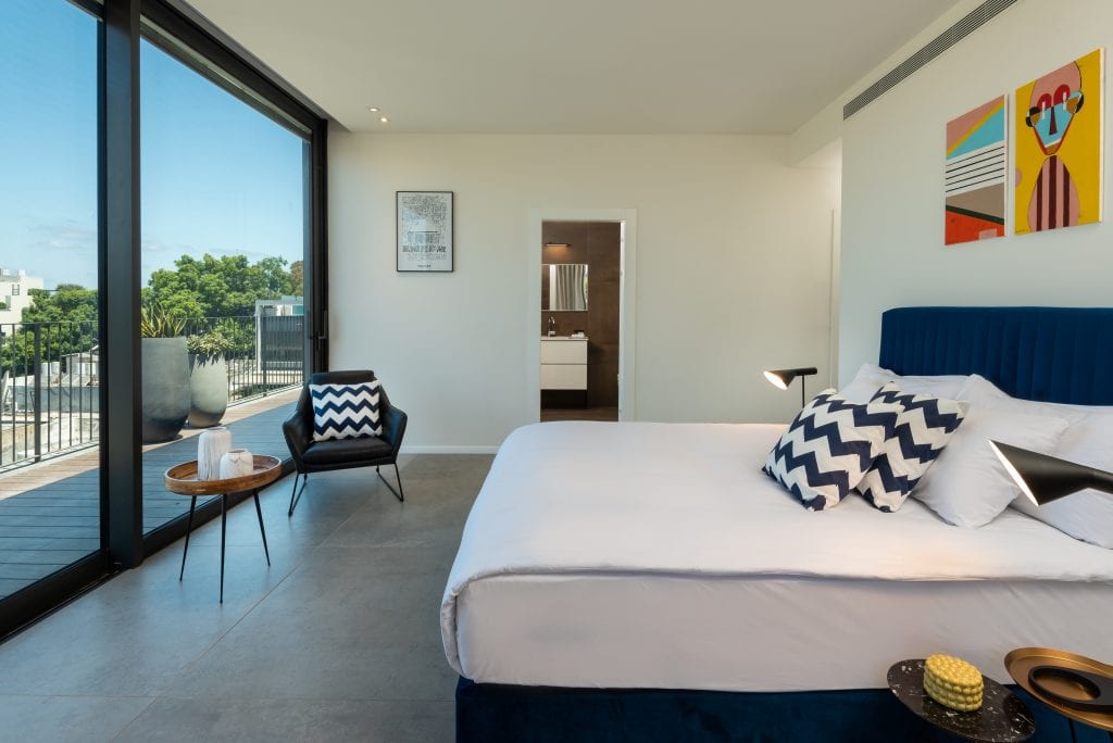 Elegant bedroom in the Four-Bedroom Penthouse at master Shenkin Tel Aviv, featuring a cozy bed and a glass door opening to the private terrace.