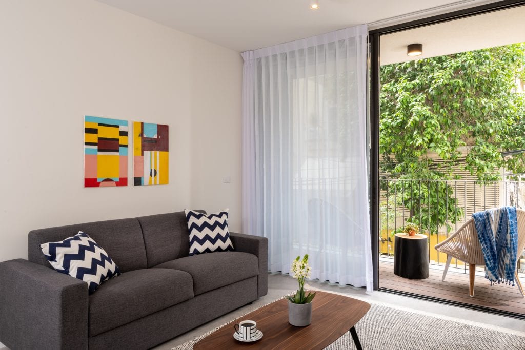 Bright and modern living room in the Two-Bedroom Apartment with Balcony at master Shenkin Tel Aviv, seamlessly connected to the outdoor balcony.