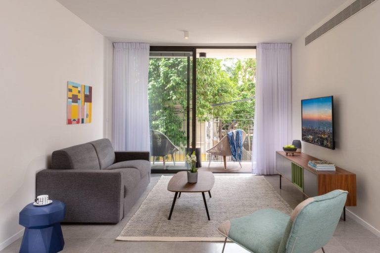 Spacious living area in the Two-Bedroom Apartment with Balcony at master Shenkin Tel Aviv, featuring a glass door leading to a private outdoor space.