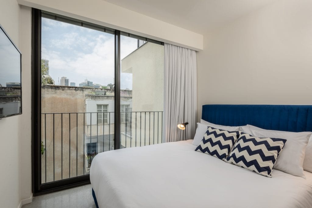 Elegant bedroom in the Four-Bedroom Apartment with Balcony at master Shenkin Tel Aviv, offering a cozy bed and access to a private outdoor space