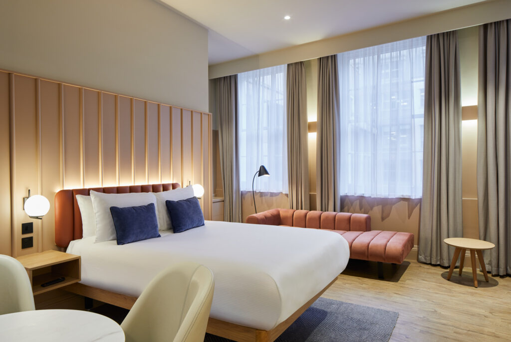 pacious studio at master Cannon London with large bed, pink sofa, tall windows with curtains, and warm, soft lighting.