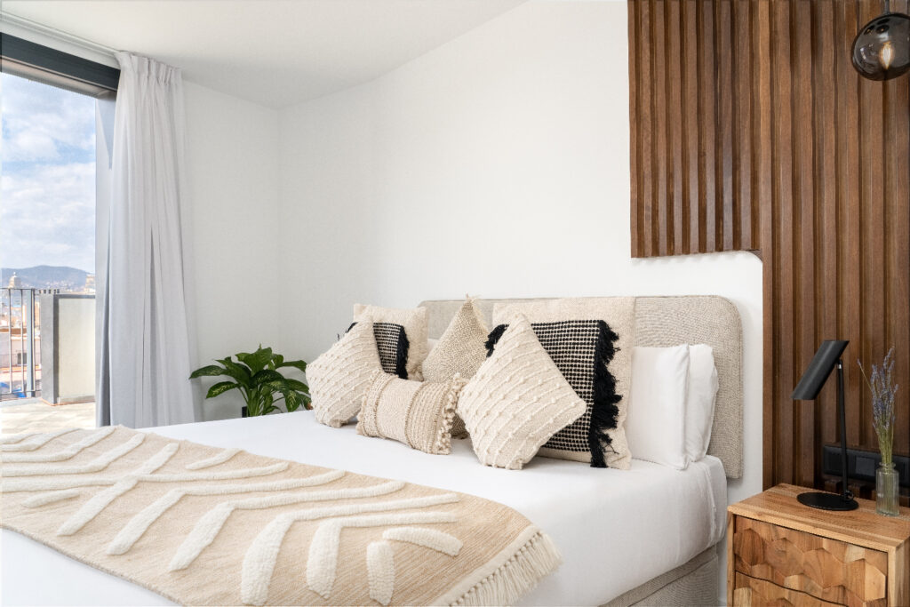 Elegant bedroom with decorative pillows, wooden accent wall, and glass doors leading to the private terrace.