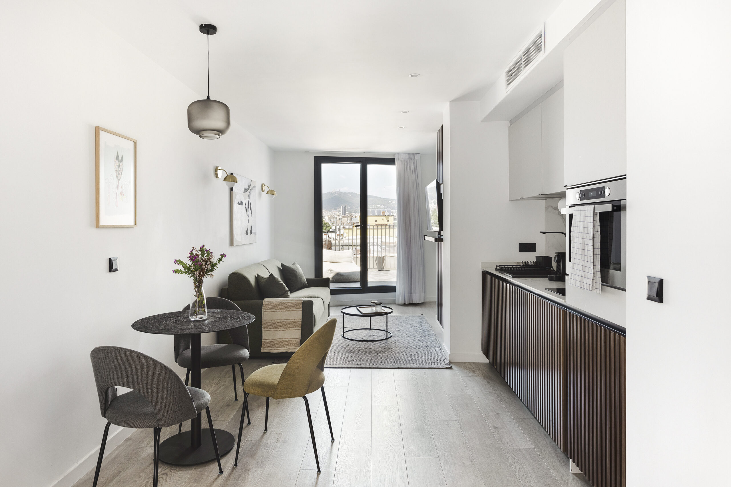 Spacious living room at master La Rambla Barcelona with sofa, dining table, fully equipped kitchen, and balcony doors with city views.