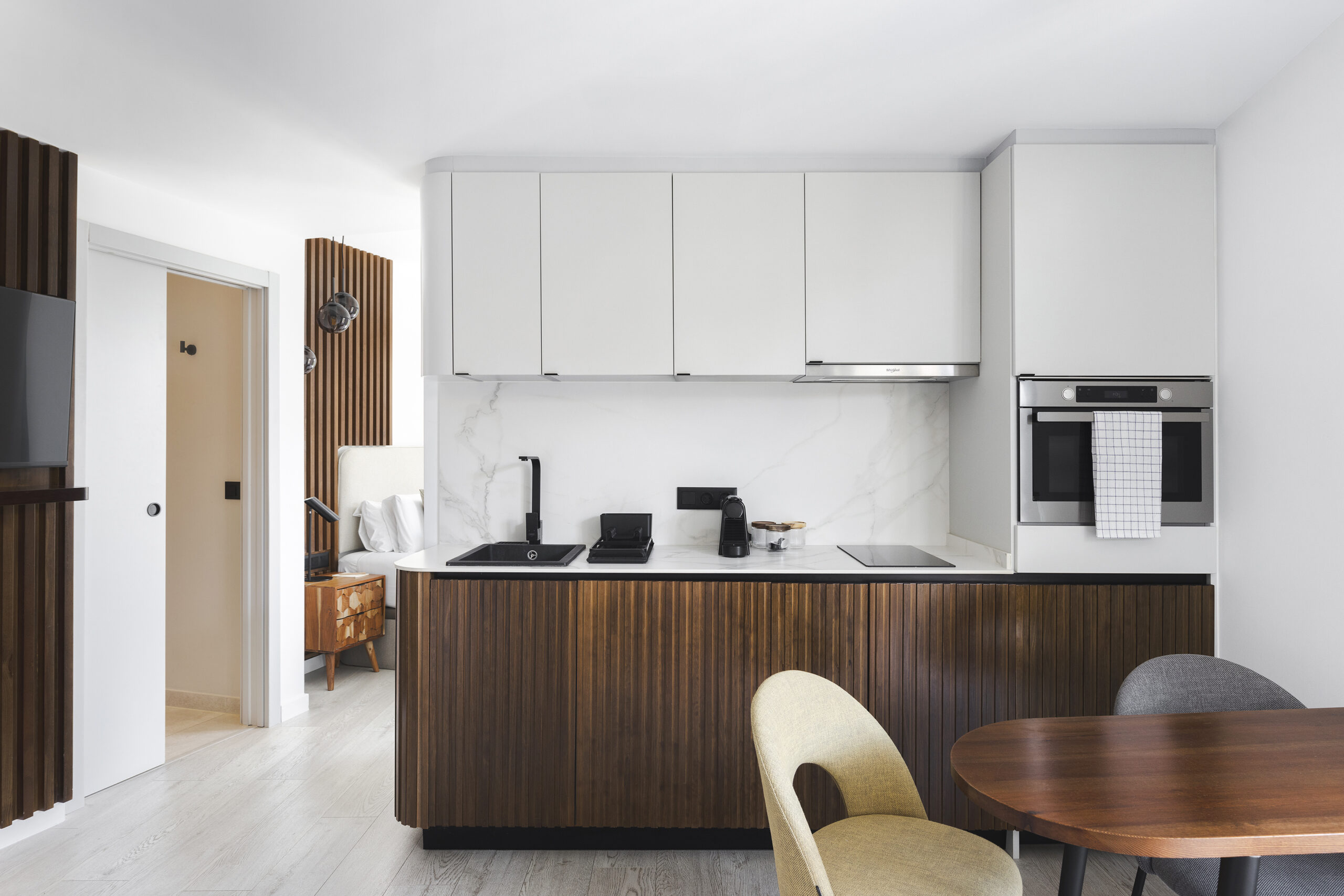 Stylish kitchen at master La Rambla Barcelona with wood-panel cabinets, marble backsplash, black sink, oven, and dining table.