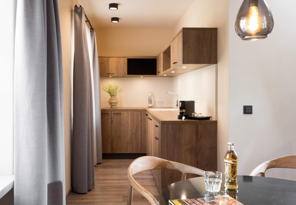 Modern kitchenette at master Linzergasse featuring wooden cabinets, ample counter space, espresso machine, and large windows with elegant curtains.