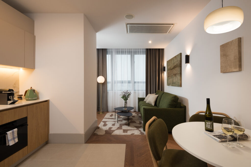 Open-plan living area at master Wola Serviced Apartments with kitchenette, dining table, and green sofa seating area