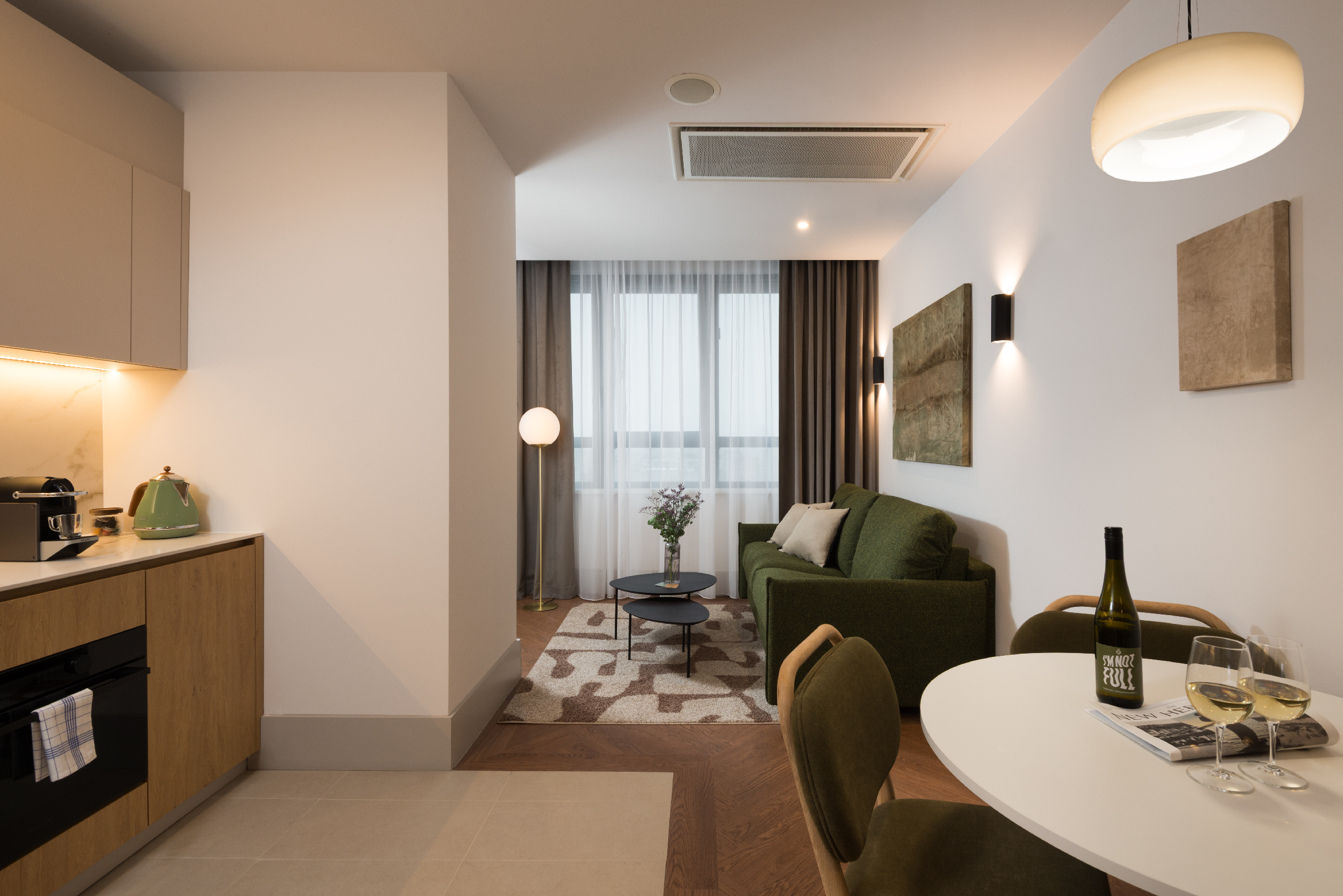 Open-plan living area at master Wola Serviced Apartments with kitchenette, dining table, and green sofa seating area