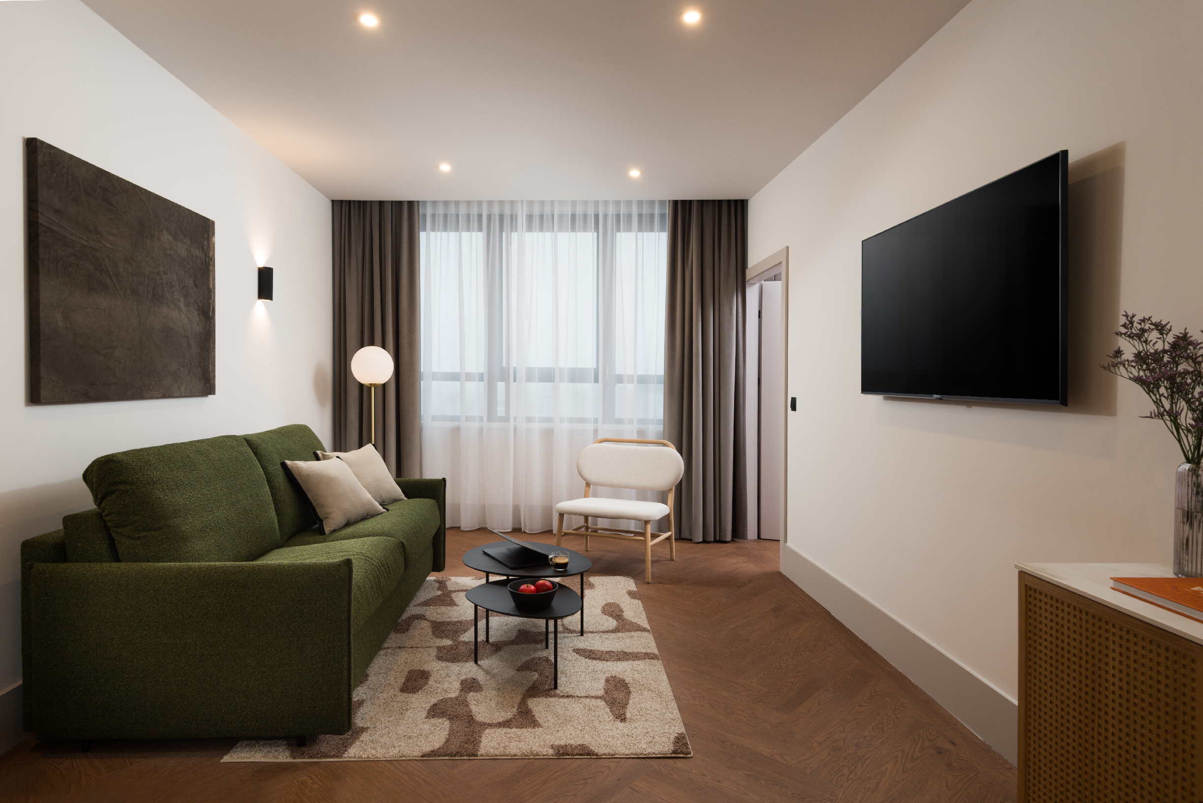 Stylish living room at master Wola Serviced Apartments featuring a green sofa, coffee table, and wall-mounted TV