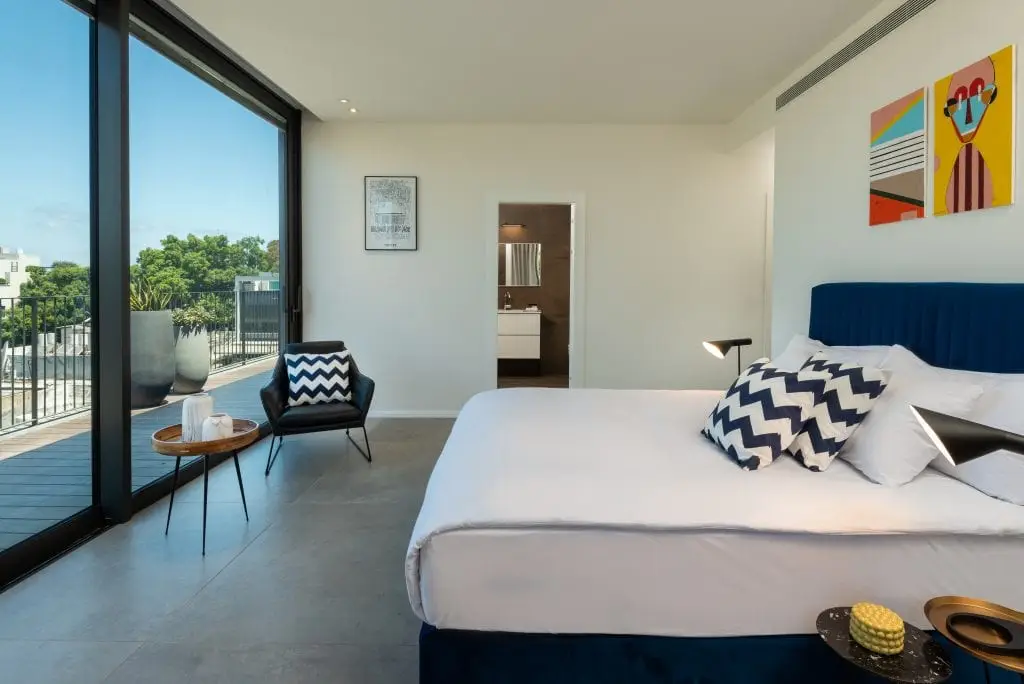 Elegant bedroom in the Four-Bedroom Penthouse at master Shenkin Tel Aviv, featuring a cozy bed and a glass door opening to the private terrace.