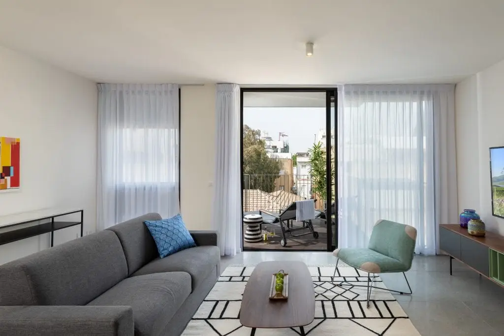Bright and spacious living area in the Three-Bedroom Apartment with Big Terrace at master Shenkin Tel Aviv, featuring a glass door leading to the outdoor terrace.