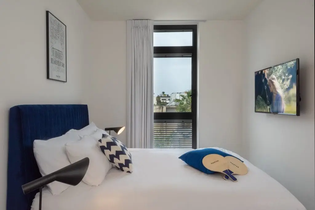 Comfortable bedroom in the Three-Bedroom Apartment at master Shenkin Tel Aviv, featuring a plush bed and a warm, inviting atmosphere.