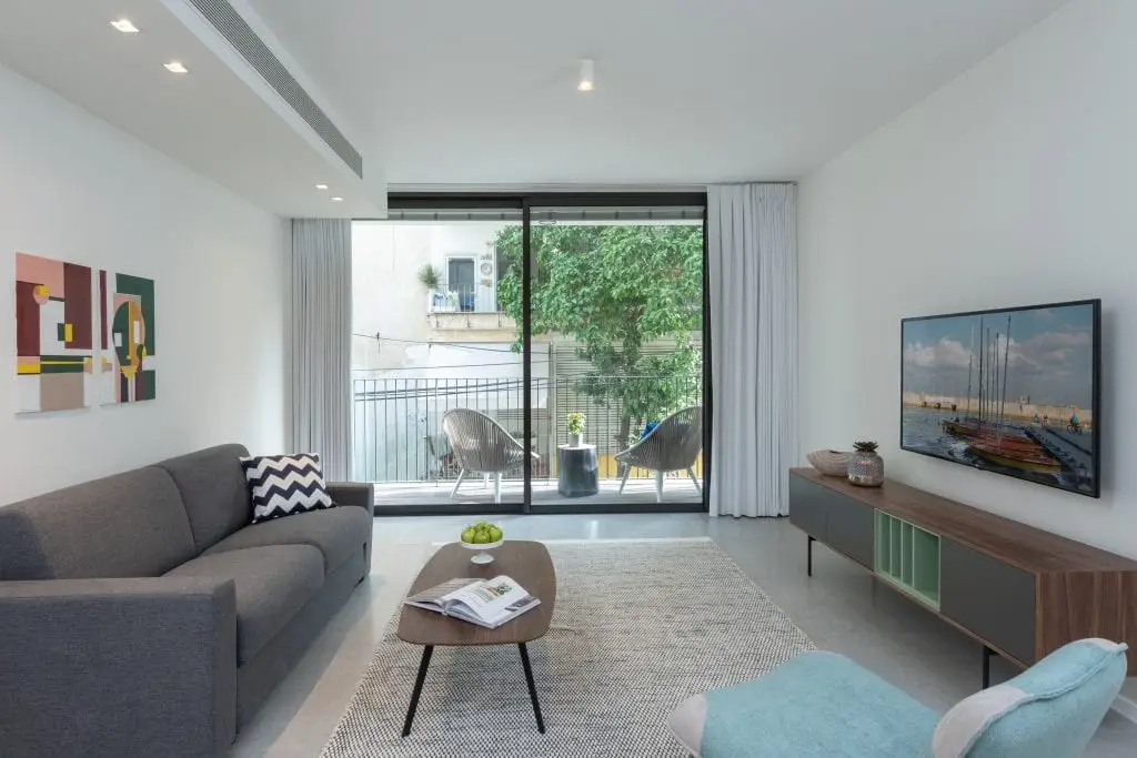 Bright and inviting living area in the One-Bedroom Apartment with Balcony at master Shenkin Tel Aviv, featuring a glass door that opens to a private balcony.