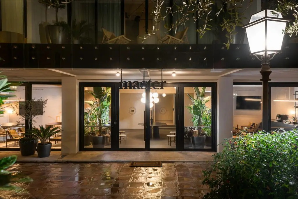 Sleek glass entrance door of master Trevi Rome Aparthotel at night, reflecting the warm glow of city lights.