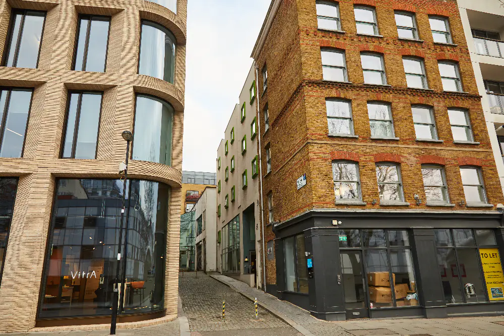 View of the street leading to master Farringdon London serviced apartments, with a large brick building, bare trees, and city life in the background.