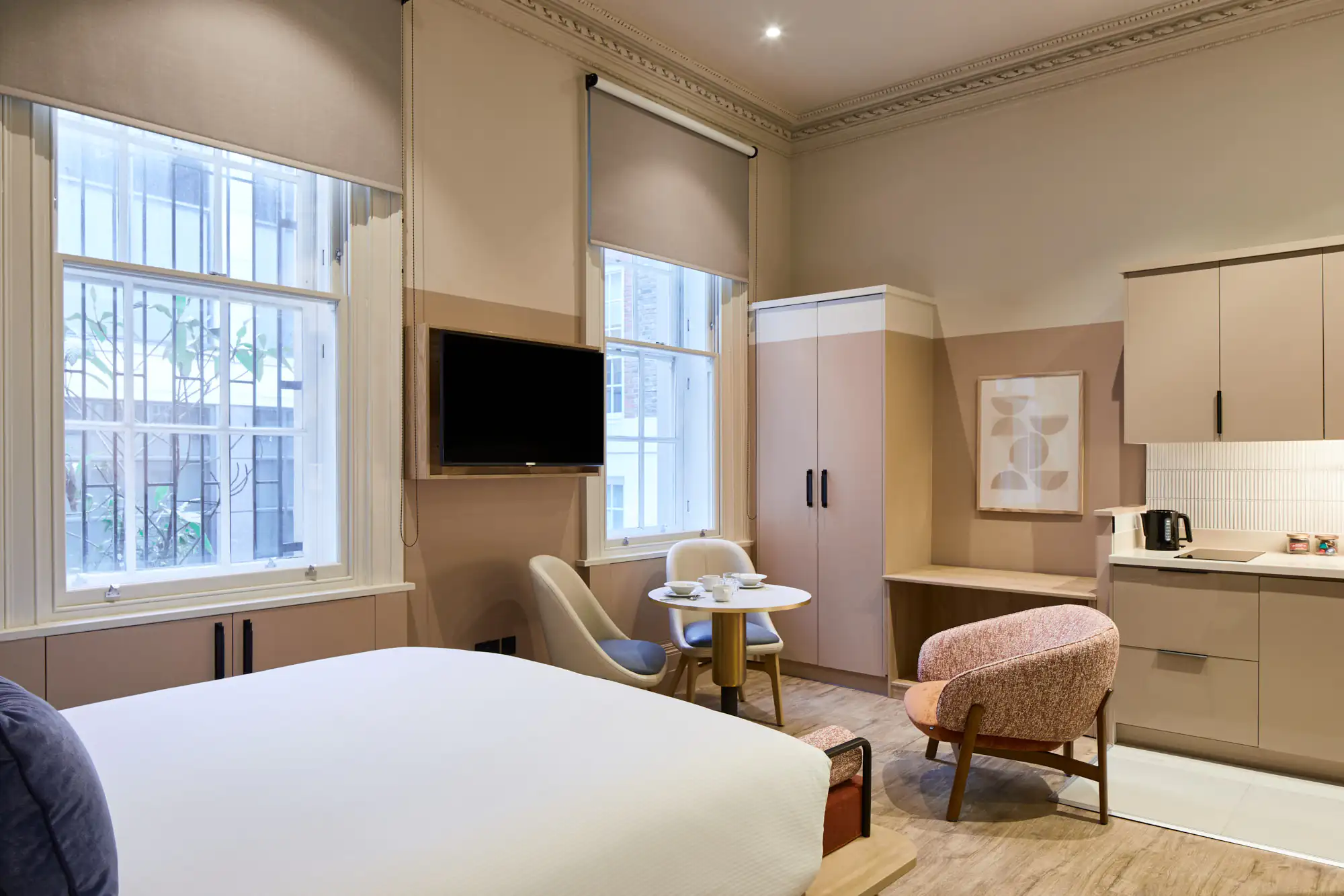 Spacious studio at master Cannon London with a modern kitchen, small dining table, comfortable bed, and elegant neutral palette accented by soft furnishings.