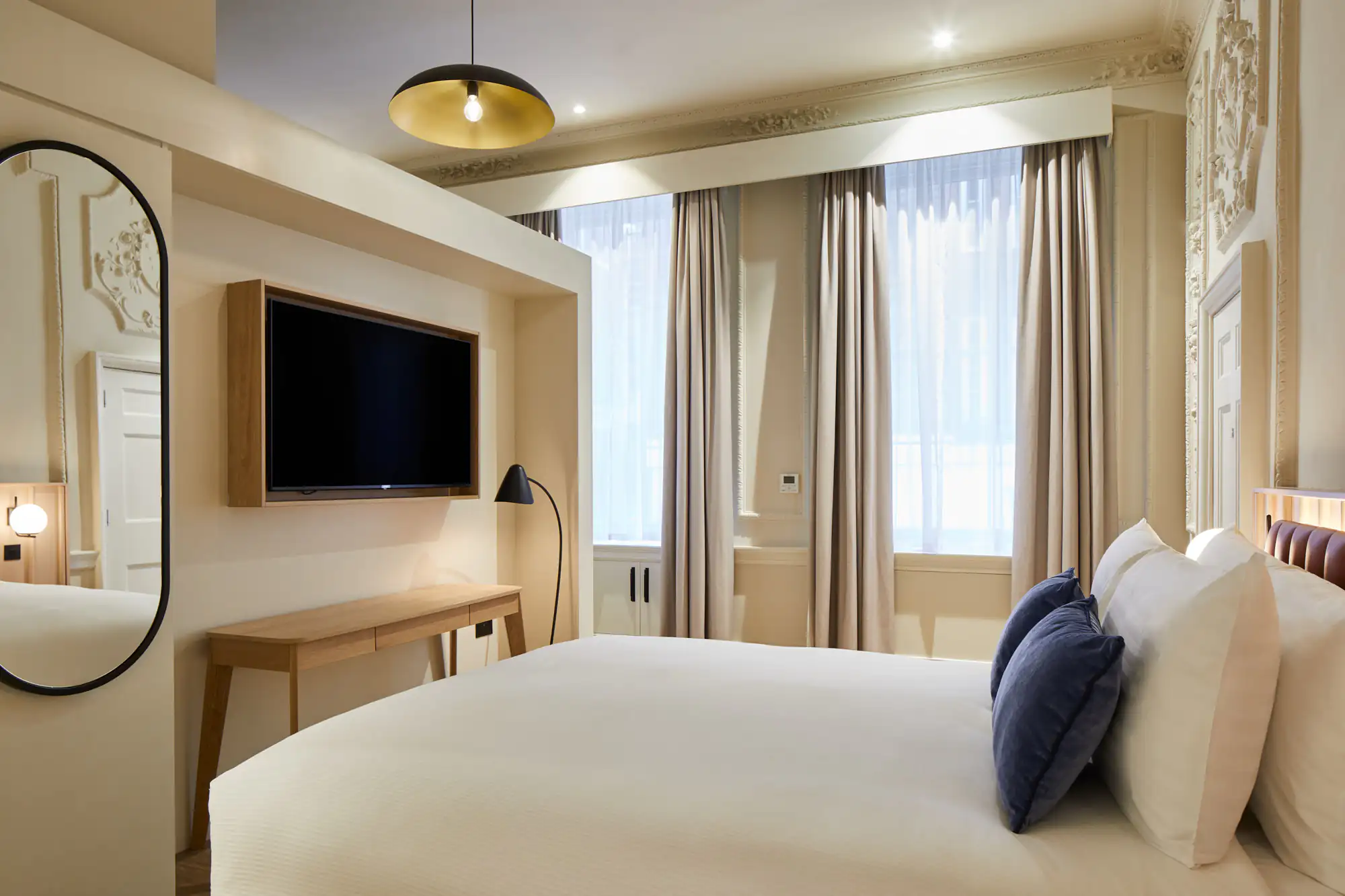 Bedroom with large bed, two blue pillows, and tall windows framed by elegant curtains and decorative wall detailing.