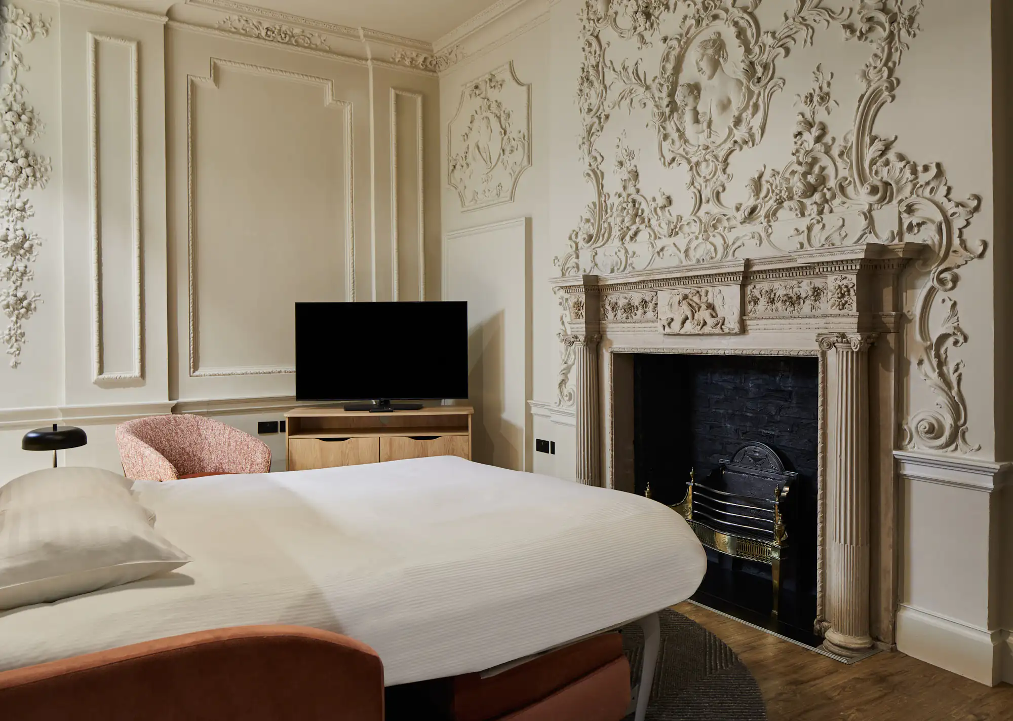 Living area with decorative fireplace, TV, and pink sofa, blending historic architecture with contemporary furnishings.