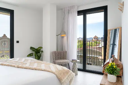 Bright and airy bedroom with two sets of balcony doors, soft neutral decor, and natural light in the One Bedroom Apartment at master La Rambla.