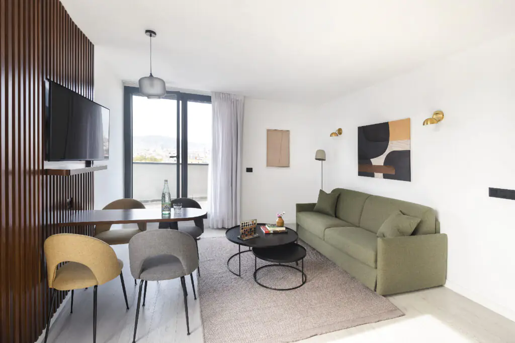 Stylish penthouse living and dining space with large TV, modern chairs, and floor-to-ceiling windows showcasing Barcelona’s skyline.