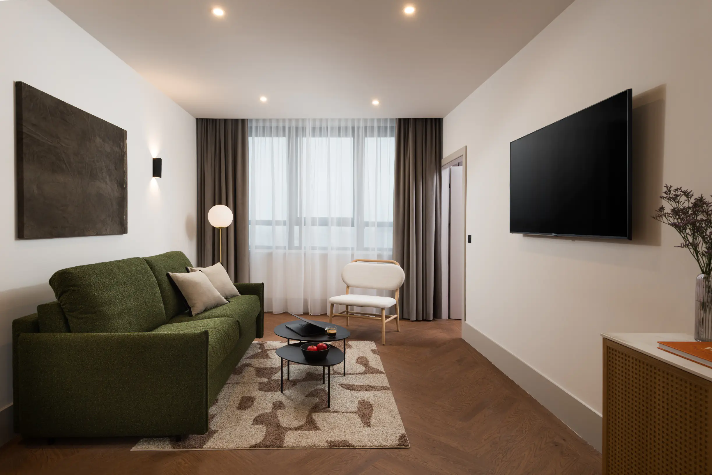 Stylish living room at master Wola Serviced Apartments featuring a green sofa, coffee table, and wall-mounted TV